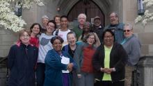 Fifteen participants at the Justice Summit 2019 Lakewood stand in front of gothic style building with flowering trees on each side